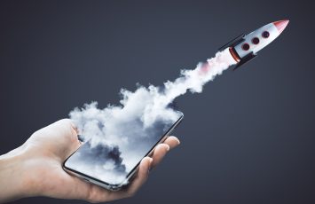 Hand holding smartphone with launching rocket on dark background. Startup and business concept